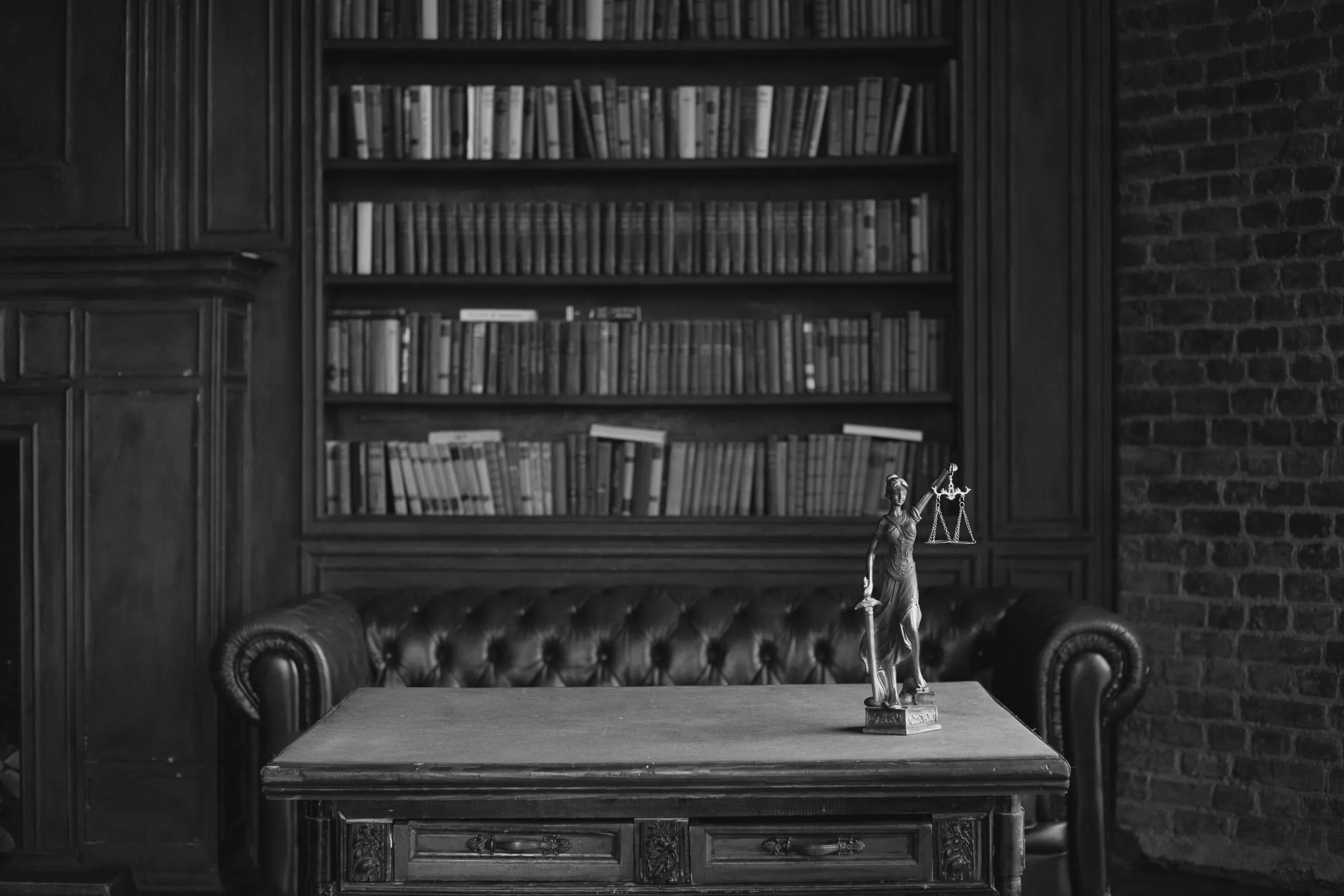 Мирна работна соба обложена со дрво: полици со стари книги, кожен тросед и работна маса со мала статуа на Правдата со вага.